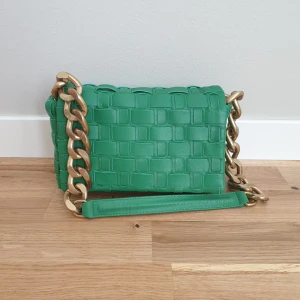 Grön axelväska med kedjedetaljer - Zara - Snygg grön axelväska med en unik flätad design och stora guldfärgade kedjor som axelrem. Väskan har en stilren look och är perfekt för att ge din outfit en färgklick. Den är tillverkad i konstskinn och har en praktisk storlek för dina dagliga behov.  L 21, H15, botten 21×5cm