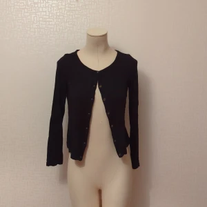 Svart kofta - Säljer en stilren svart kofta med långa ärmar och knappar framtill. Perfekt för både vardag och fest. Den är i bra skick och passar till det mesta i garderoben. Är i stl 170 men passar xs/s utmärkt. Litte nopprig i tyget