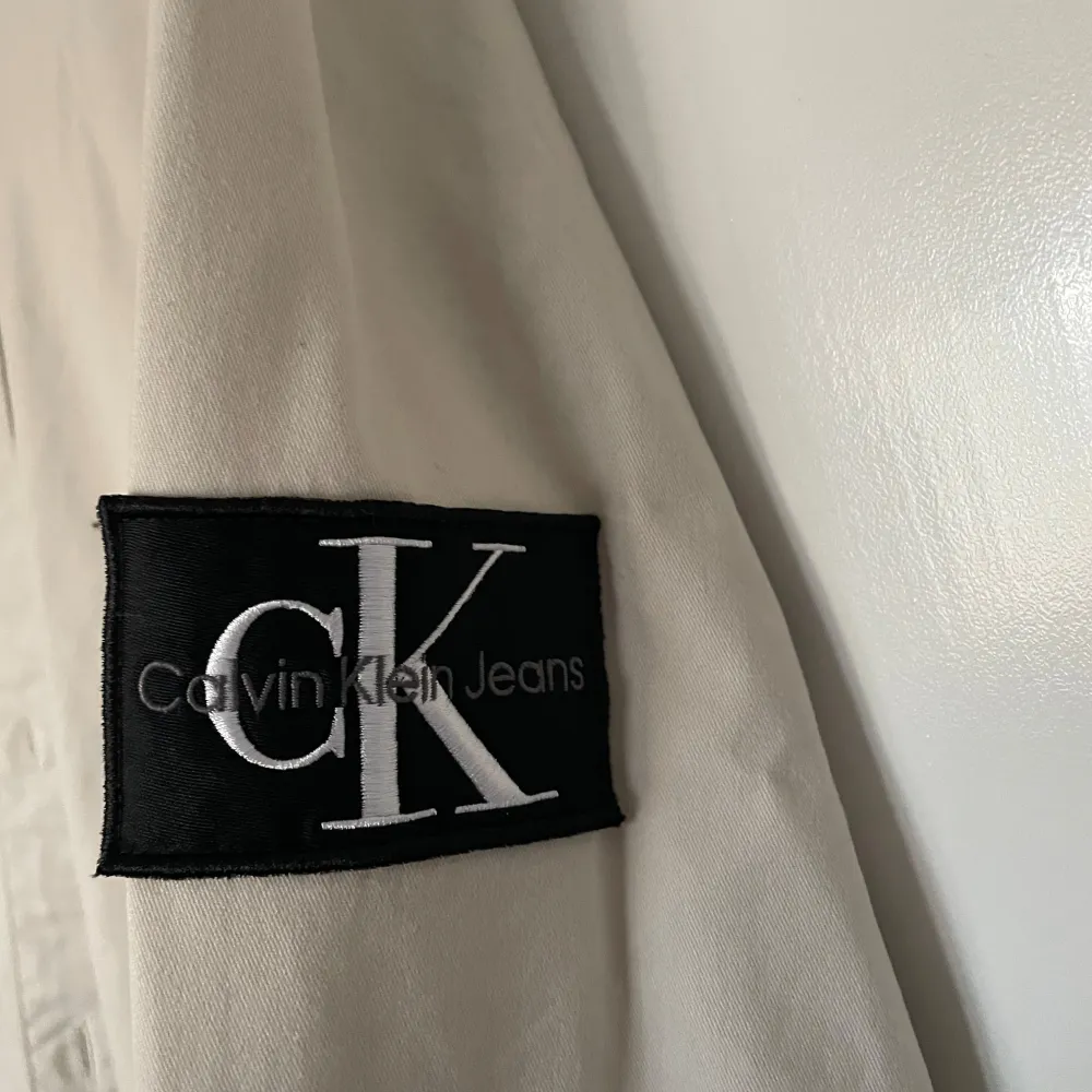 Säljer en stilren beige skjorta från Calvin Klein Jeans i storlek L. Skjortan har långa ärmar och en klassisk krage. Den är i regular fit och har en diskret logga på ärmen. Perfekt för både vardag och fest! Nypris 999kr. Skjortor.