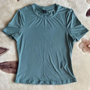 Grön t-shirt i skims-material - Säljer en stilren grön t-shirt från Shein i stl S. Den är tillverkad av 87% polyamid och 13% elastan, vilket gör den superbekväm och stretchig. Skims-material!  Perfekt för vardagsbruk, basplagg eller tränings plagg. Kortärmad+figurnära & i nyskick!
