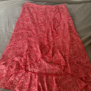 Röd blommig kjol från SHEIN - Säljer en superfin röd kjol från SHEIN med ett sött blommigt mönster. Kjolen har en volangdetalj längst ner och en praktisk dragkedja i sidan. Perfekt för både vardag och fest! 🌸