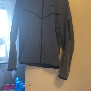 Mörk blå hoodie från Nike - Säljer en blå tech fleece hoodi från Nike i storlek S. Den har en dragkedja framtill och en huva för extra skydd mot väder och vind. Perfekt för höst och vår, med en stilren design och långärmade ärmar. Jackan är i bra skick och redo för nya äventyr!