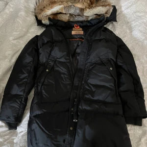 Svart vinterjacka från Parajumpers - Säljer en snygg och varm svart vinterjacka från Parajumpers. Jackan har en pälsluva och är perfekt för kalla vinterdagar. Den har en dragkedja och knappar framtill samt praktiska fickor. Jackan är i storlek XS och har en slim fit passform.❄️ Som ny