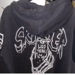 Säljer en svart hoodie med en cool skelettdesign. Den har en stor ficka fram och tryck på ärmarna. Perfekt för en avslappnad stil eller för att sticka ut på festen!