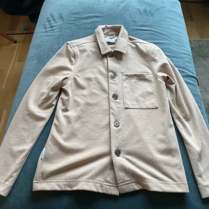En tjock skjorta  - Säljer en tjock skjorta i beige färg. Säljer den eftersom den är för liten. Inga defekter.
