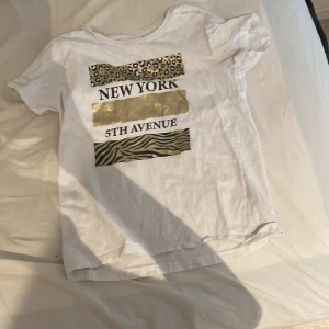 Vit t-shirt från Firefly med New York-tryck - Säljer en vit t-shirt som e köpt från Intersport i storlek 158/164. T-shirten har ett coolt tryck med texten 'New York' och '5th Avenue' samt mönster i leopard och zebra. Perfekt för en avslappnad och trendig look! 🗽✨