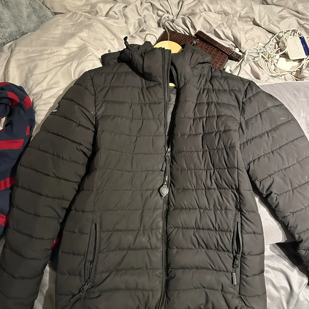 Säljer en svart pufferjacka från Superdry. Den är perfekt för kyliga dagar med sin vadderade design och har en praktisk huva. Jackan har dragkedja framtill och två fickor med dragkedjor. Den är i mycket bra skick! Herrstorlek men kan användas av alla❄️❄️. Jackor.