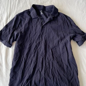 Svart pikétröja från H&M - Säljer en mörkblå pikétröja från H&M i storlek M. Tröjan är i bomull och har korta ärmar. Perfekt för både vardag och fest. Den är i bra skick men skrynklig. Väldigt bekväm att ha på sig. Passformen är normal och den har en klassisk krage med knappar. Frågor? Skriv!