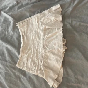 Beige kjol med volang - Säljer en superfin beige kjol med volangdetaljer. Kjolen är kort och passar perfekt till både vardag och fest. Materialet känns som linne och ger en naturlig look. 