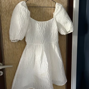 Studentklänning - Säljer en superfin vit klänning med puffärmar. Den är kort och har en härlig struktur i tyget som ger en extra touch. Perfekt för sommarens alla fester eller kanske till midsommar! Klänningen är i nyskick och passar perfekt för dig som vill ha något unikt och stilrent. 💖Den är även öppen i ryggen. 