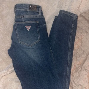 Blå jeans från Guess - Snygga blå jeans från Guess med skinny fit och midwaist. Klassisk femficksdesign med dragkedja och knapp framtill. Perfekta för en stilren look. Aldrig använda! 