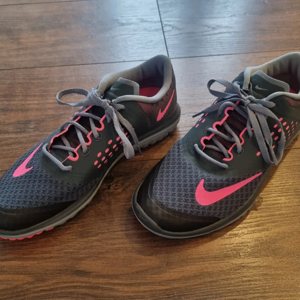 Helt nya snygga grå Nike löparskor med rosa detaljer och snörning. Skorna har en mönstrad sula för bra grepp och en sportig design. Perfekta för träning eller en aktiv vardag. US 7, UK 4,5 EUR 38. NIKEARTNR: 684667-005. Kengät.