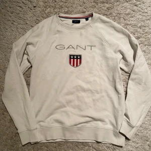 Vit sweatshirt från GANT - Köp via PostNord !!! Storlek 170 /15 years Sitter som S .      Säljer en stilren vit sweatshirt från GANT med broderad logga och emblem på bröstet. Tröjan har långa ärmar och rund halsringning. Perfekt för en avslappnad stil. Inga defekter väldigt fint skick kostade 900