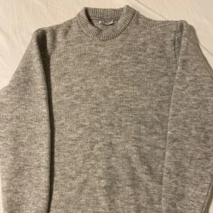 Grå stickad tröja från Zara - Säljer en stilren grå stickad tröja från Zara. Tröjan har en klassisk rund hals och långa ärmar, perfekt för kyligare dagar. Den är mjuk och bekväm, idealisk för både vardag och avslappnade tillfällen.