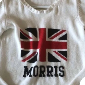 Vit stickad tröja från Morris - Säljer en vit stickad tröja från Morris med ett stort Union Jack-mönster och texten 'Morris' på framsidan. Tröjan har långa ärmar och en rund halsringning. Perfekt för en stilren och trendig look.
