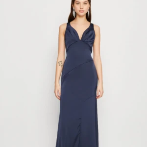 Marinblå långklänning med v-ringning - Elegant marinblå långklänning med v-ringad hals och ärmlös design. Perfekt för en stilfull kväll med sin figurnära passform och mjuka material. Klänningen har en diskret dragkedja i ryggen för enkel påklädning. Aldrig använd, endast provad.