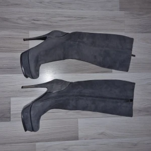 Grå vintage stövlar från Yves Saint Laurent - Eleganta grå vintage stövlar från Yves Saint Laurent i mocka med hög klack och dragkedja på sidan. Perfekta för en stilren look.