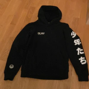 Svart hoodie med japanskt tryck - Säljer en svart hoodie från The Boys med coolt japanskt tryck på ärmen och ryggen. Hoodien har en stor ficka fram och en bekväm huva. Perfekt för en avslappnad stil. Säljer den för pga ingen användning 🔥 Man kan se att den är lite använd på ena sidan med lite färg pga olycka, som säkert går att ta bort med vanish‼️ Annars jätteskön och inga skador eller hål på den! 