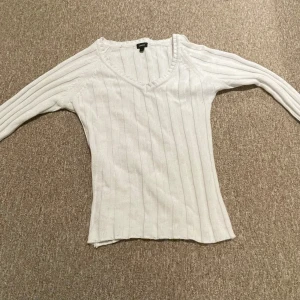 Vit ribbad tröja med v-ringning - Säljer en stilren vit ribbad tröja med v-ringning. Tröjan har långa ärmar och en bekväm passform som passar perfekt till både jeans och kjol. Den är insydd så passar som storlek M!!!Perfekt för kyligare dagar!