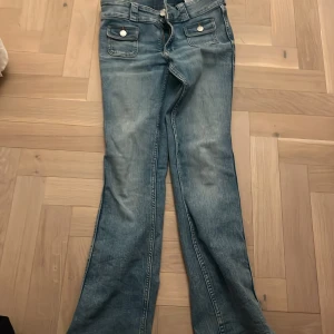 Blå jeans med fickdetaljer - Snygga blå jeans med framträdande fickor och knappar. De har en dragkedja och bälteshällor, vilket gör dem praktiska och stilrena. 