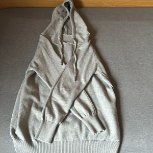 Grå merinoull hoodie - Säljer en stilren grå merinoull hoodie med långa ärmar och ribbade muddar. Perfekt för en avslappnad look. Den har en klassisk huva med dragsko för justering.