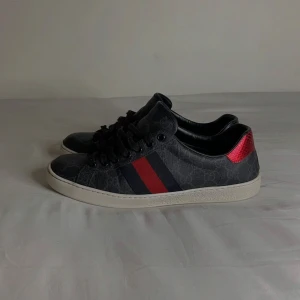 Svarta gucci ace sneakers - Snygga svarta sneakers från Gucci med röda och blå detaljer på hälen. Skorna har en vit sula och klassisk snörning. Riktigt fräscha och passar  under alla tillfällen. Inget og medföljs 🌎