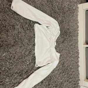 Vit ribbad långärmad topp - Säljer en vit ribbad långärmad topp i barnstorlek 8Y. Perfekt för en stilren och bekväm look. Toppen har en enkel design med rund halsringning.