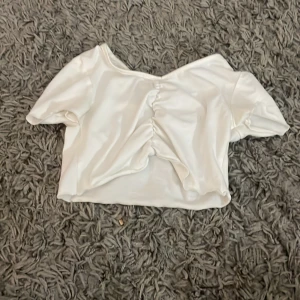 Vit kortärmad topp för barn - Säljer en söt vit kortärmad topp för barn. Toppen har en fin rynkad detalj framtill och är gjord i ett mjukt material. Perfekt för sommarens varma dagar!