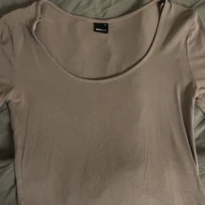 Beige topp från Gina Tricot - Säljer en stilren beige topp från Gina Tricot i storlek M. Toppen har korta ärmar och en rund halsringning, perfekt för en enkel och avslappnad look.