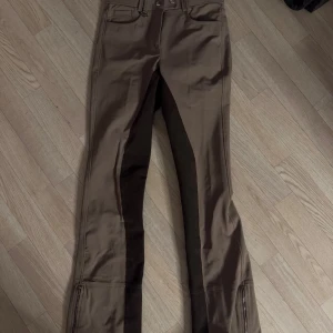 Bruna ridbyxor med dragkedja bootcut - Helt oanvända snygga bruna ridbyxor med dragkedja vid bensluten och dubbla knappar i midjan. Byxorna har förstärkningar i mörkare ton på insidan av benen och praktiska fickor både fram och bak💕 