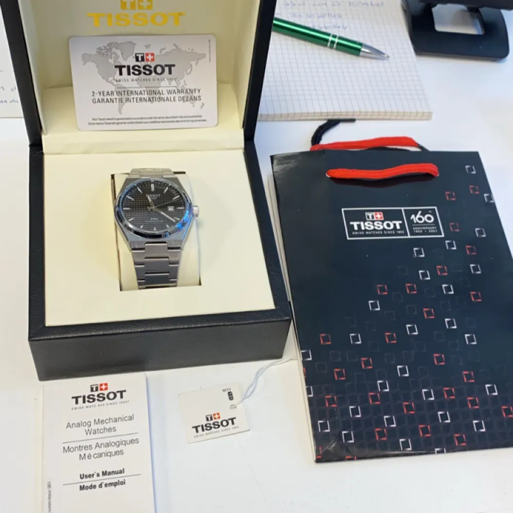 Snygg Tissot PRX Powermatic 80 med en stilren svart urtavla och datumvisning. Klockan har ett robust armband i silverfärgat stål och kommer i originalförpackning med manual och garantikort. Perfekt för den som söker en elegant och tidlös accessoar.. Asusteet.