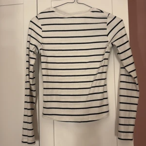 Vit och svart randig långärmad tröja - Säljer en stilren vit tröja med svarta ränder. Tröjan är långärmad och har en ribbad struktur som ger en skön passform. Perfekt för en avslappnad look.