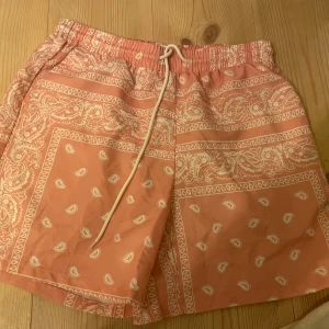 Mönstrade shorts med snörning - Snygga shorts i en ljus rosa  färg med ett vitt paisleymönster. De har en bekväm passform med elastisk midja och snörning för justering. Perfekta för sommarens varma dagar.