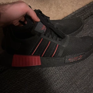 Svarta Adidas NMD med röda detaljer - Snygga svarta Adidas NMD sneakers med röda detaljer. Skorna har en modern design med bekväm passform och snörning. Perfekta för en stilren look.