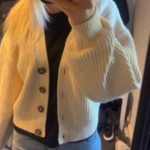 Beige stickad kofta med knappar - Säljer en mysig beige stickad kofta med stora knappar framtill. Koftan har en ribbad struktur och långa ärmar, perfekt för kyligare dagar. Passar bra till jeans eller kjol, andvänd cirka 3 gånger, ny skick