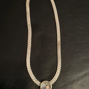 Silverfärgat halsband med glittrig sten - Elegant silverfärgat halsband med en stor, glittrig sten i mitten. Halsbandet har en robust kedja och en säker låsning. Perfekt för att ge en touch av glamour till din outfit.