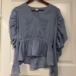 Blå blus med puffärmar  - Blå blus från ”visual Clothing project”. Skulle säga att den är lite ljusare i färgen än vad som framgår på bilderna. Inte mycket använd , fint skick! Storlek S