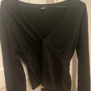Svart omlottopp från Gina Tricot - Snygg svart omlottopp från Gina Tricot med långa ärmar. Perfekt för en stilren look. Toppen har en v-ringad design och knytning i midjan för en smickrande passform.