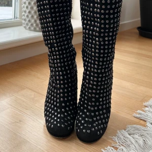 Svarta stövlar med nitar och klack - Snygga svarta stövlar dekorerade med silverfärgade nitar över hela ytan. De har en hög, spegelblank klack som ger en extra touch av glamour. Perfekta för att göra ett statement!