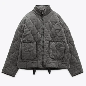 Grå quiltad jacka från Zara  - Säljer en grå quiltad jacka från Zara med dragkedja framtill och två stora fickor. Jackan har en hög krage och långa ärmar, perfekt för kyligare dagar. Den har en unik quiltad design som ger en stilren look.