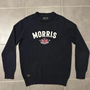 Morris Stickad Tröja Navy S - Storlek M på lappen men passar S. Säljer en snygg mörkblå tröja från Morris med vit text och ett tryck av en brittisk flagga på framsidan. Tröjan har långa ärmar och ribbade muddar vid ärmslut och nederkant. Perfekt för en stilren look!