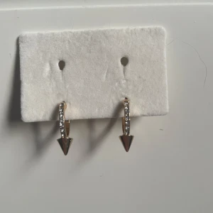 Guldörhängen med strass och spetsig detalj - Snygga guldörhängen med en rad av glittrande strass och en spetsig hängande detalj. Perfekta för att ge en edgy touch till din stil. Lätta att matcha med andra smycken.