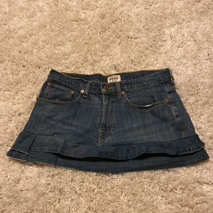 Jeanskjol  - Snygg jeanskjol  i klassisk blå denim. Kjolen har en kort längd med volangdetalj längst ner och femficksdesign. Perfekt för en avslappnad stil. Egensydd!