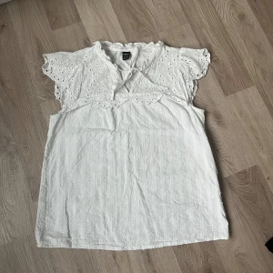 Vit blus med spetsdetaljer - Säljer en söt vit blus från Shein med spetsdetaljer på ärmarna och ett diskret prickigt mönster. Blusen har en knytning framtill och korta ärmar med volangkant. Perfekt för en somrig look! Blusen har mörk fläck vid sidan (se bild), vet ej om det går bort i tvätt men märks inte av.