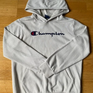 Beige hoodie från Champion - Säljer en beige hoodie från Champion med deras ikoniska logga broderad på bröstet. Tröjan har en klassisk känguruficka och en bekväm huva. Perfekt för en avslappnad stil.