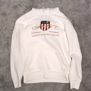 Vit GANT hoodie - Säljer en snygg GANT hoodie med deras klassiska logga och texten 'American Sportswear' på framsidan. Säljer för att den blev för liten och jag behöver cash 