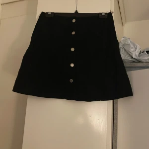 Svart kjol med knappar - Snygg svart kortkjol med knappar framtill. Perfekt för en stilren look. Passar bra till olika tillfällen och kan enkelt matchas med olika toppar.