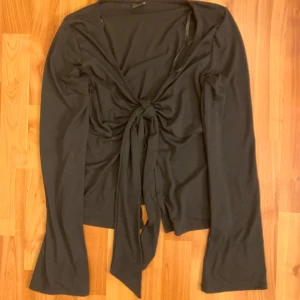 Svart knytblus från Gina Tricot - Säljer en stilren svart blus från Gina Tricot med knytning framtill. Blusen har långa ärmar och är perfekt för en chic look. Passar bra till både jeans och kjol. Perfekt för höst och vår!