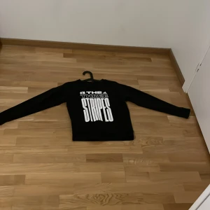 Svart långärmad tröja från Adidas pris kan diskuteras  - Säljer en svart långärmad tröja från Adidas med texten 'THE THREE STRIPES' i vitt på framsidan. Perfekt för en sportig look eller avslappnad stil.
