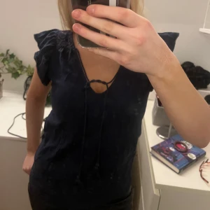 Svart blus med knytband - Snygg svart blus med knytband vid halsen och volangdetaljer vid ärmarna. Perfekt för en stilren look.